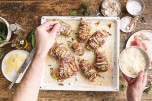 Sfornare e servire le Patate Hasselback con emmental e prosciutto di San Daniele ben calde.