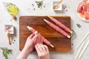 Arrotolare su un bastoncino di legno il carpaccio di manzo e il Prosciutto di San Daniele