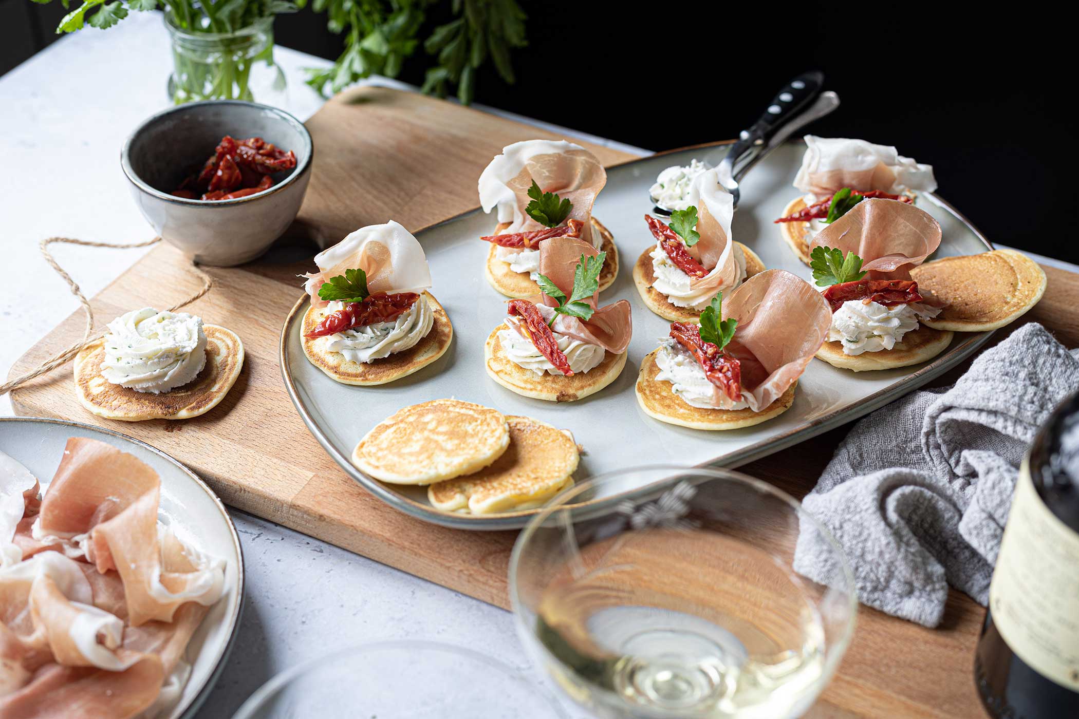 Blins con Prosciutto di San Daniele, crema di robiola al prezzemolo e pomodori secchi