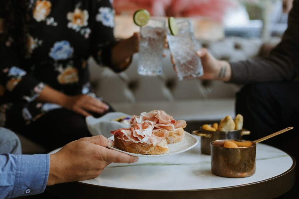 amici seduti al tavolo imbandito con cocktail, fette di pane e prosciutto e altri snack