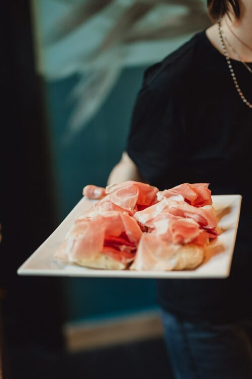 donna con maglia nera che tiene tra le mani un piatto bianco con fette di pane e prosciutto di san daniele