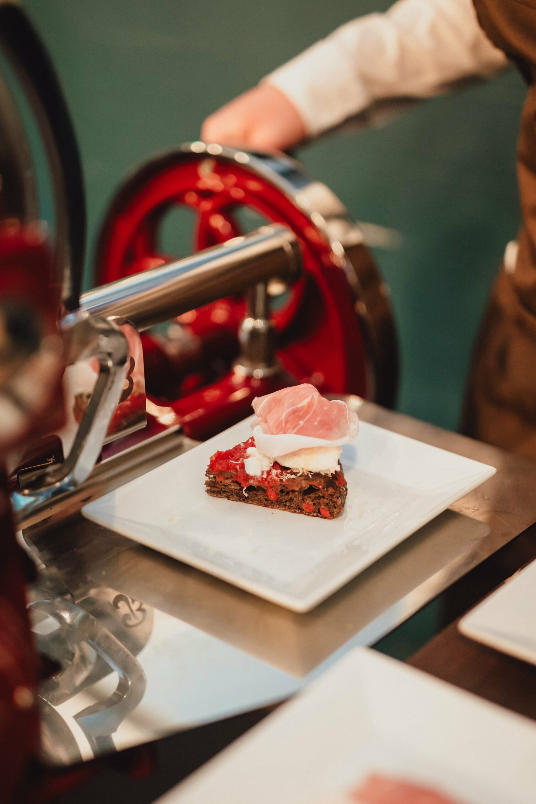piatto bianco con fetta di pane e di prosciutto di san daniele con affettatrice sullo sfondo in occasione di una degustazione organizzata