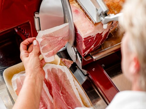 vendita prosciutto san daniele. Primo piano di persona che affetta una coscia di prosciutto con l'affettatrice