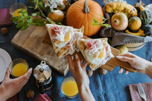 tavola imbandita con zucche, bicchieri di aranciata e tranci di focaccia con prosciutto di san daniele