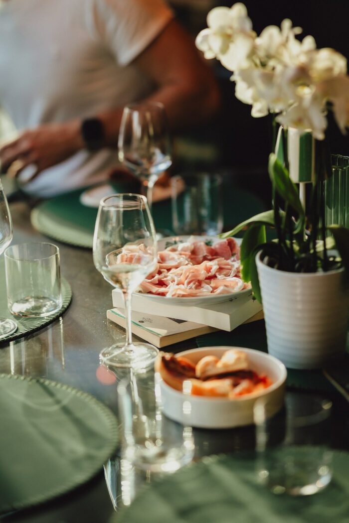 Tavola imbandita con piatti a base di prosciutto e calici di sakè