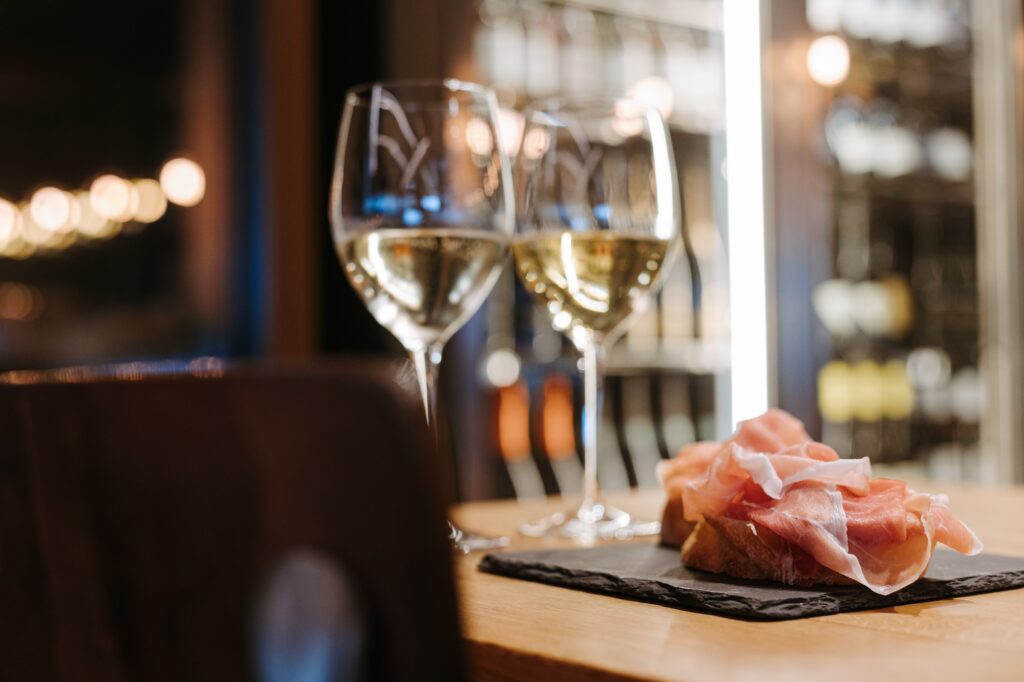 primo piano di fetta di pane con prosciutto di san daniele e calici di vino bianco sullo sfondo