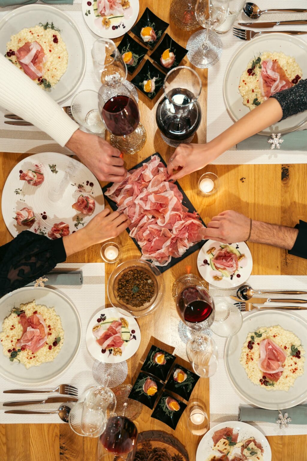 tavola di natale imbandita con persone che prendono delle fette di prosciutto di san daniele nel corso dell'aperitivo