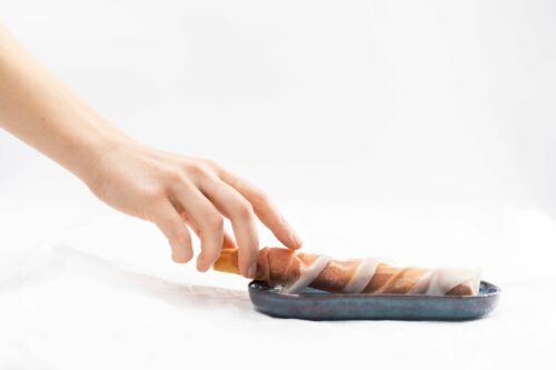 Mano che prende un grissino avvolto nel Prosciutto di San Daniele su un piattino