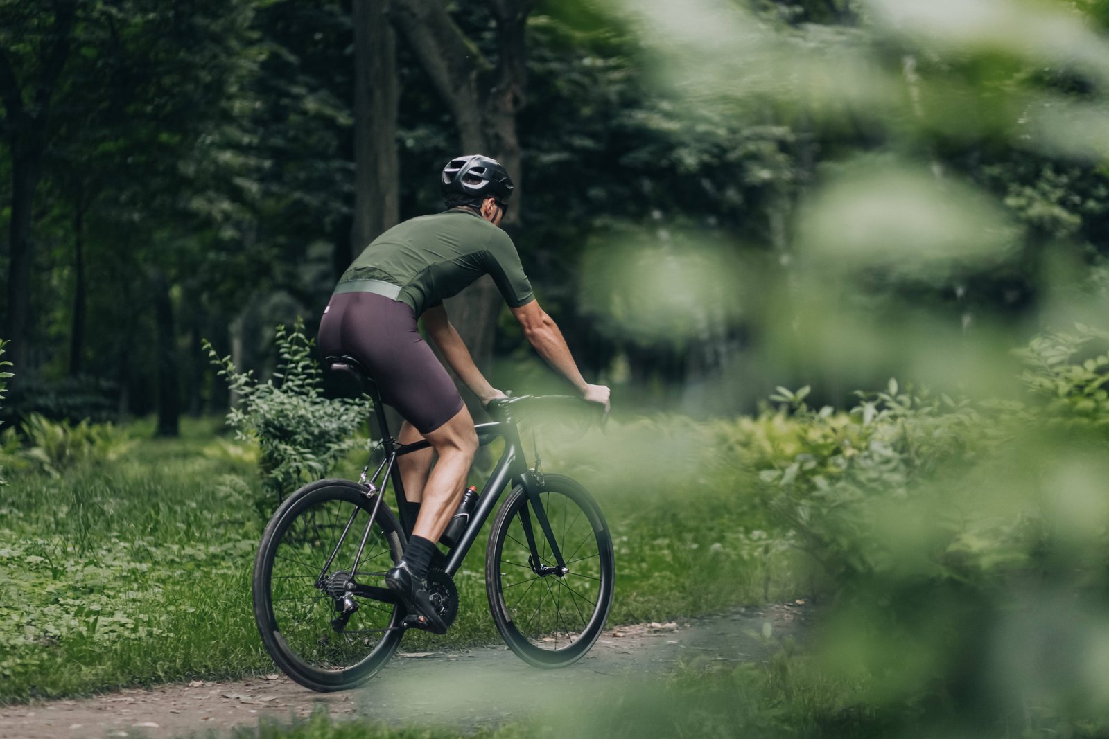 Ciclista di spalle su sentiero nel bosco durante allenamento outdoor, sport per cui il Prosciutto di San Daniele è un alleato nutrizionale
