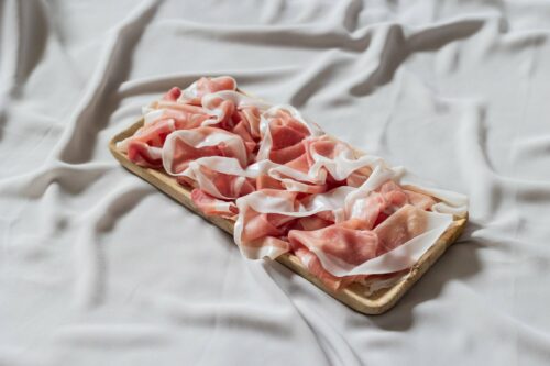 Fette arricciate di Prosciutto di San Daniele DOP con bordo di grasso su tagliere di legno