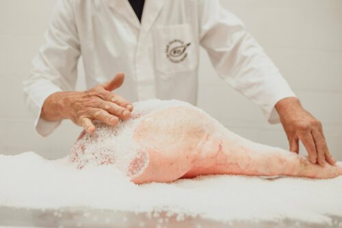 Mastro prosciuttaio cosparge sale marino sulla coscia durante la salatura del Prosciutto di San Daniele DOP