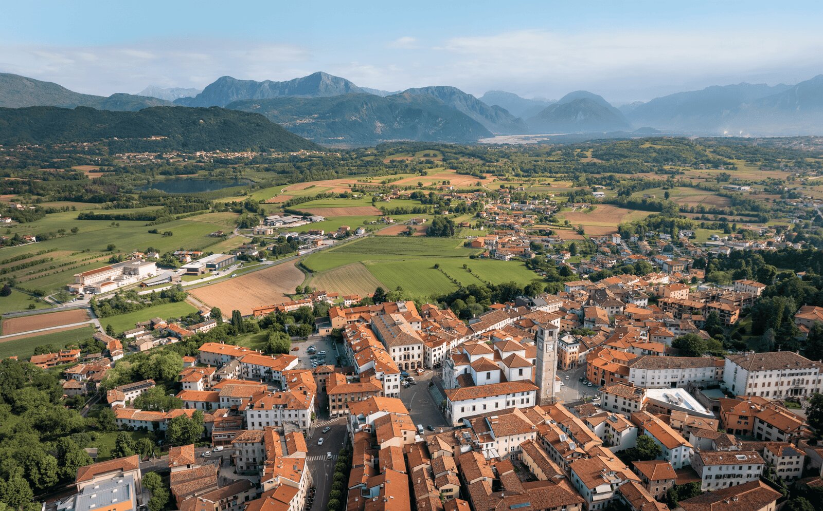 Veduta aerea di San Daniele del Friuli con la pianura coltivata e le Alpi Carniche sullo sfondo, microclima del territorio del Prosciutto di San Daniele DOP