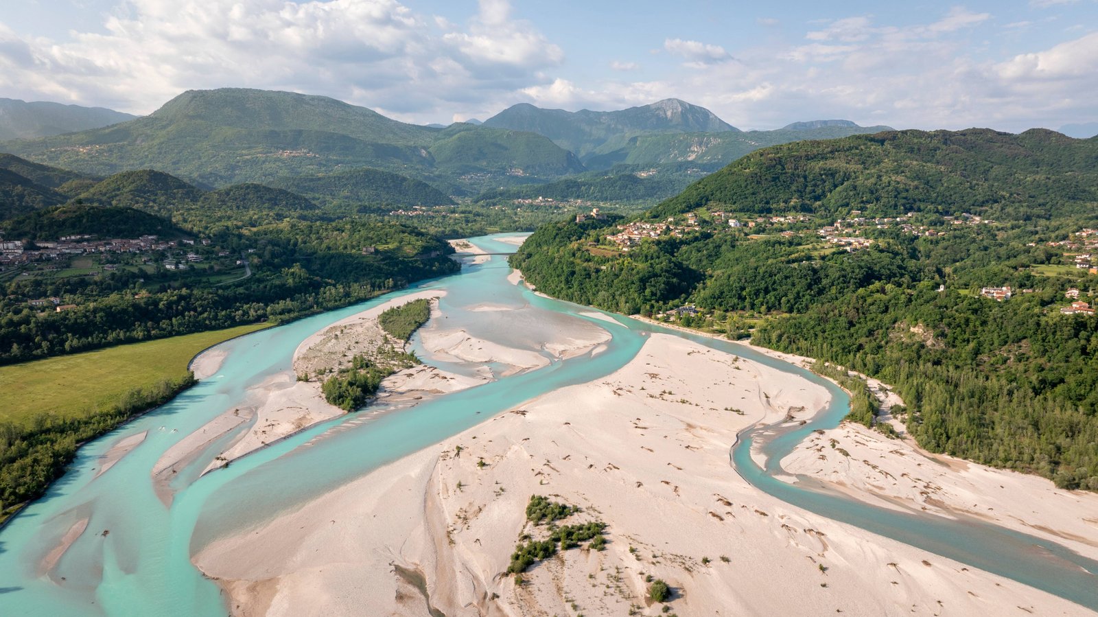 Veduta aerea del fiume Tagliamento che scorre accanto a un borgo collinare, nel microclima che favorisce la stagionatura del San Daniele DOP