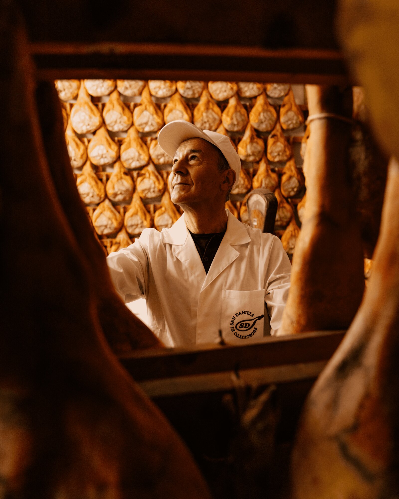 Mastro prosciuttaio in camice bianco osserva i prosciutti nella sala di stagionatura del Prosciutto di San Daniele DOP