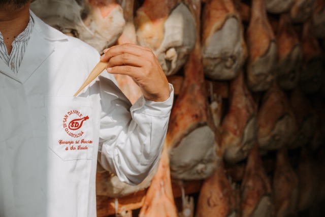 Dettaglio della puntatura sul Prosciutto di San Daniele DOP con logo del Consorzio ricamato sul camice dell'operatore