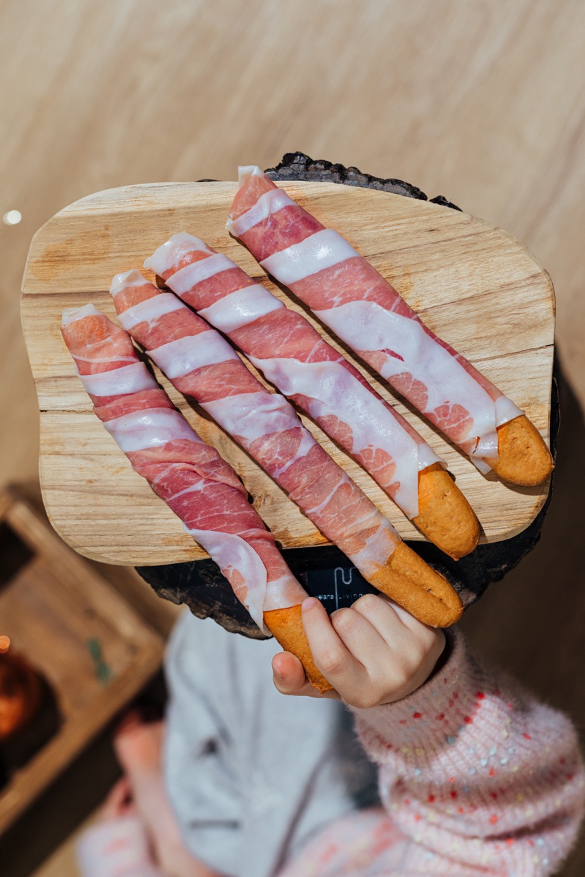 Grissini avvolti nel Prosciutto di San Daniele DOP retti da una mano di bambino, snack sano e naturale