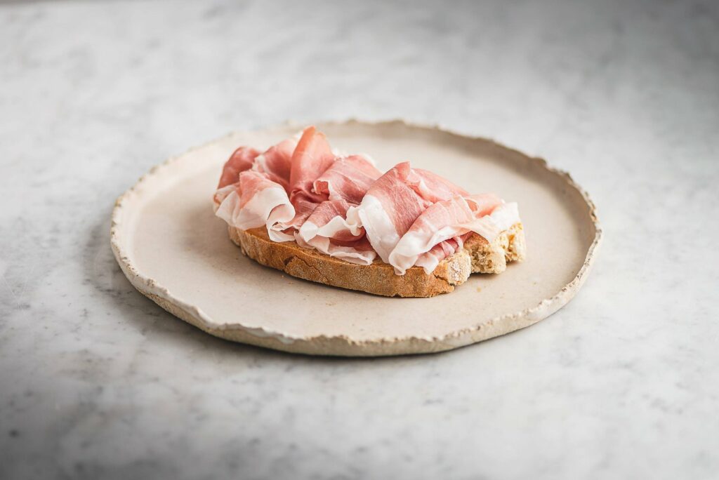 Fetta di pane con Prosciutto di San Daniele DOP, a richiamare i cereali dell’alimentazione dei suini