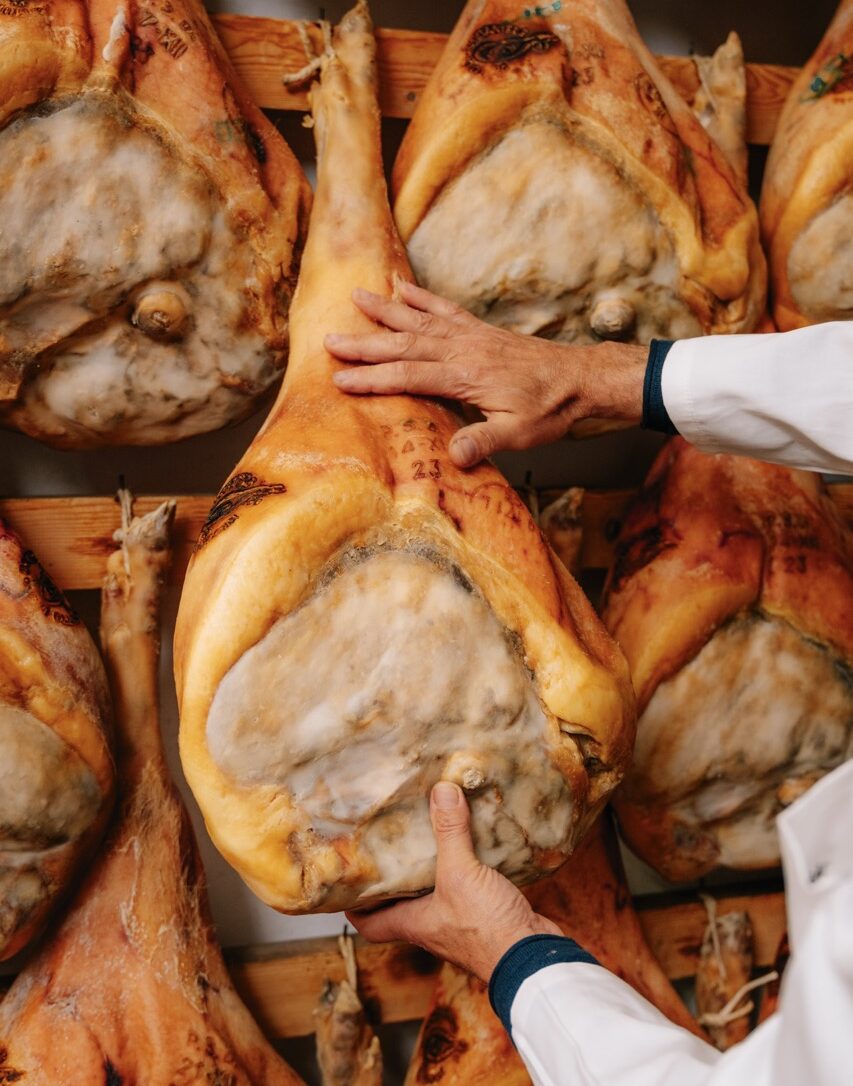 Mani che valutano forma e consistenza di un Prosciutto di San Daniele DOP stagionato, con il contrassegno a fuoco sulla cotenna